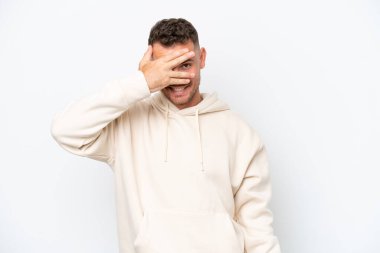 Beyaz arka planda izole edilmiş beyaz tenli yakışıklı bir adam. Gözleri elleriyle kaplıyor ve gülümsüyor.