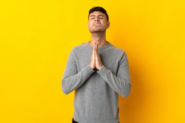 Sarı arka planda izole genç Kolombiyalı adam avuç içlerini bir arada tutuyor. İnsan bir şey ister.