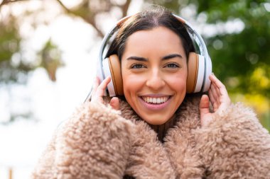 Genç esmer kadın açık havada müzik dinliyor.