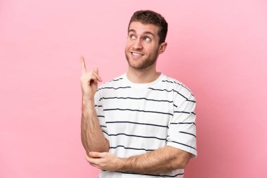 Pembe arka planda izole edilmiş genç beyaz adam harika bir fikre işaret ediyor.