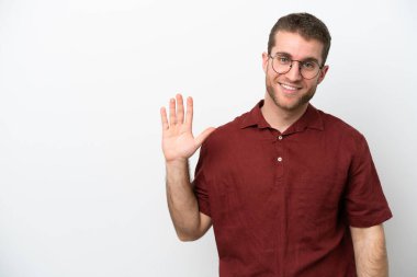 Beyaz arka planda izole edilmiş genç beyaz bir adam mutlu bir ifadeyle selamlıyor.