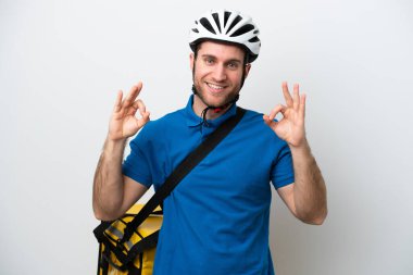 Beyaz arka planda izole edilmiş termal sırt çantalı beyaz bir adam parmaklarıyla iyi bir işaret gösteriyor.