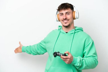Beyaz arka planda izole edilmiş bir bilgisayar oyunu kontrolörüyle oynayan yakışıklı genç adam davet edilmek için ellerini yana uzatıyor.
