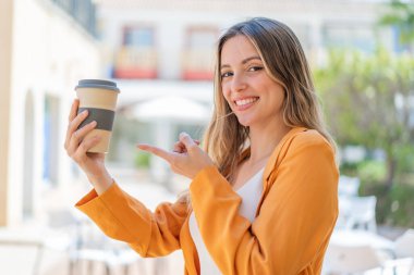Genç ve güzel bir kadın açık havada kahve tutuyor ve onu doğrultuyor.