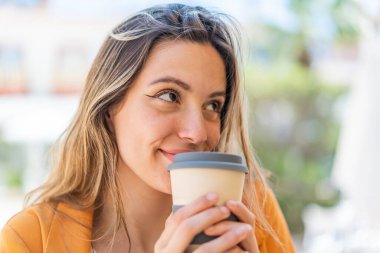 Dışarıdaki güzel kadın elinde kahve tutuyor.