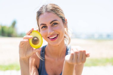 Avokado tutan genç sarışın bir kadın. Eli ile gelmesi için davet ediyor. Gelmene sevindim.