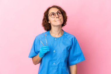 İngiliz dişçi kadın, pembe arka planda izole edilmiş aletleri tutuyor.