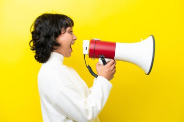 Arjantinli genç bir kadın sarı arka planda izole edilmiş bir şekilde megafondan bağırıyor.