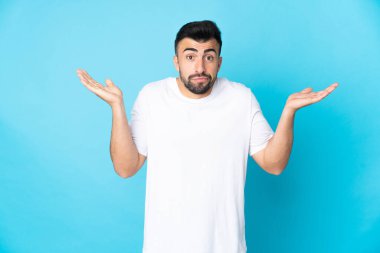İzole edilmiş mavi arka planı olan beyaz bir adam ellerini kaldırırken şüpheye düşüyor.