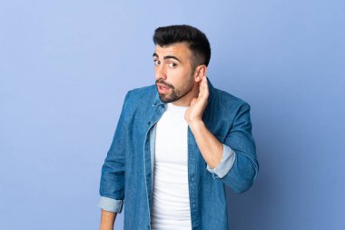 İzole edilmiş mavi arka planda beyaz bir adam. Kulağına elini sürerek bir şeyler dinliyor.