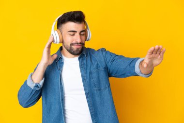 İzole edilmiş sarı arka plan üzerinde beyaz bir adam müzik ve dans dinliyor.