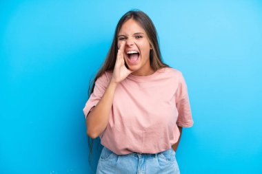 Mavi arka planda izole edilmiş genç beyaz kadın ağzı açık bağırıyor.