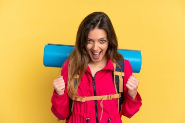 Sarı arka planda saklanmış büyük sırt çantalı genç dağcı galibiyeti kutluyor.