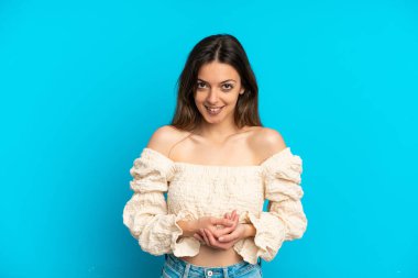 Mavi arka planda izole edilmiş genç beyaz kadın gülüyor.