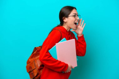 Mavi arka planda izole edilmiş genç beyaz kadın ağzı sonuna kadar açık bağırıyor.