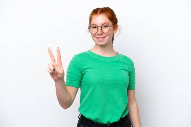 Beyaz arka planda izole edilmiş genç bir kadın gülümsüyor ve zafer işareti gösteriyor.