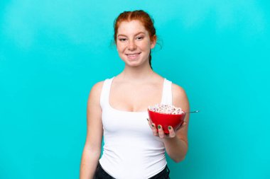 Kırmızımsı bir kadın elinde bir kase mısır gevreği tutarken mavi arka planda bolca gülümsüyor.