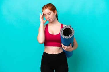 Genç spor kırmızısı kadın yoga derslerine giderken elinde mavi arka planda başağrısı olan bir minder tutuyordu.