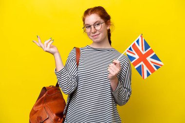 Sarı arka planda izole edilmiş bir Birleşik Krallık bayrağı tutan genç İspanyol kadın davet edildiği için elini yana uzatıyor.