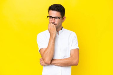 Soyutlanmış sarı arka planı olan yakışıklı bir genç. Şüpheleri var.