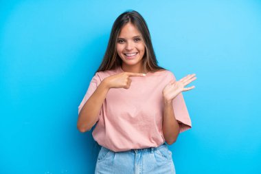 Mavi arka planda izole edilmiş genç beyaz kadın bir ilan vermek için avucunun içinde hayali bir fotokopi makinesi tutuyor.
