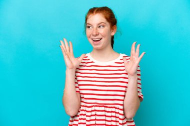 Mavi arka planda yalıtılmış, yüzü şaşırmış genç bir kadın.