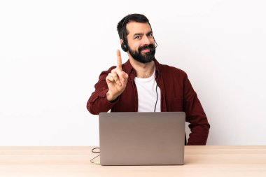 Tele-pazarlamacı beyaz adam kulaklıkla çalışıyor ve dizüstü bilgisayarla parmağını kaldırıyor..