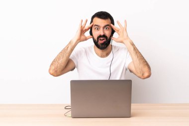 Tele pazarlamacı beyaz adam kulaklıkla ve dizüstü bilgisayarla sürpriz ifadeyle çalışıyor..