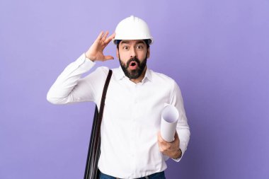 Miğferli genç bir mimar. Mor arka planda, sürpriz bir ifadeyle izole edilmiş planları tutuyor.