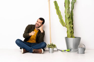 Bahçıvan içeride yerde oturuyor. Telefon hareketleriyle ön tarafı işaret ediyor.