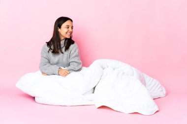 Genç melez kadın pijamasını giymiş yerde oturuyor yan tarafa bakıyor ve gülümsüyor.