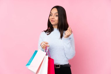 Soyutlanmış pembe arka planda alışveriş çantasıyla genç bir kadın para hareketi yapıyor.