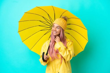 Yağmura dayanıklı paltosu ve şemsiyesi olan genç melez kadın gülümserken yukarı bakıyor.