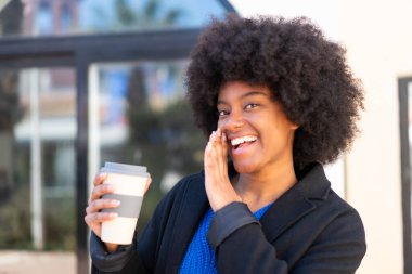 Afro-Amerikalı bir kız açık havada kahve alıp bir şeyler fısıldıyor.