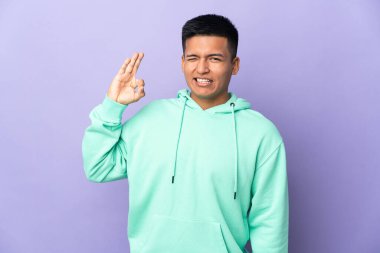 Mor arka planda izole edilmiş genç Ekvadorlu adam parmaklarıyla tamam işareti gösteriyor.
