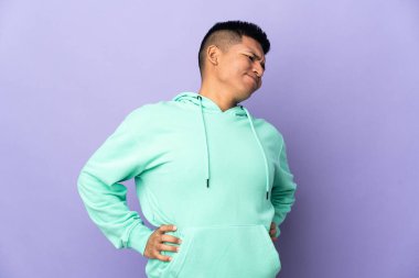 Genç Ekvadorlu bir adam mor arka planda izole edilmiş, gayret gösterdiği için sırt ağrısı çekiyor.