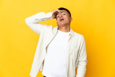 Genç Ekvadorlu, sarı arka planda izole edilmiş. Önüne bakarken sürpriz jest yapıyor.