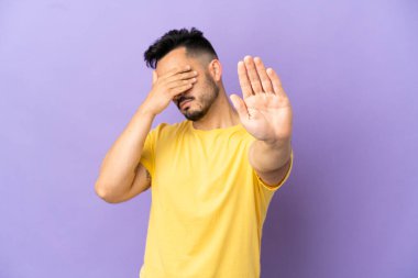 Mor arka planda izole edilmiş genç beyaz adam jesti durduruyor ve yüzünü kapatıyor.