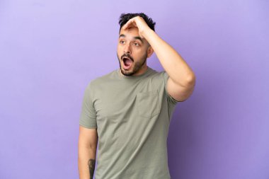 Mor arka planda izole edilmiş genç beyaz adam yan tarafa bakarken sürpriz jest yapıyor.
