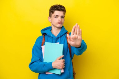 Genç Rus öğrenci, sarı arka planda izole edilmiş. Durma hareketi yapıyor.