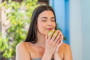 Genç, güzel Brezilyalı bir kadın açık havada elinde elma tutuyor.