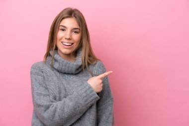 Young caucasian woman isolated on pink bakcground pointing to the side to present a product