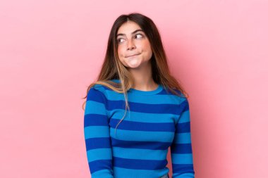 Pembe arka planda izole edilmiş genç beyaz kadın yukarı bakarken şüpheleri var.