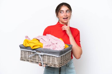 Young caucasian woman holding a clothes basket isolated on white background thinking an idea while looking up