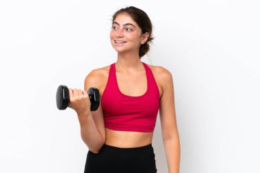 Beyaz arka planda halter kaldıran genç beyaz kadın yan tarafa bakıyor ve gülümsüyor.