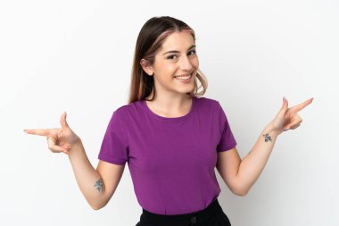 Beyaz arka planda izole edilmiş genç beyaz kadın parmak uçlarını işaret ediyor ve mutlu.