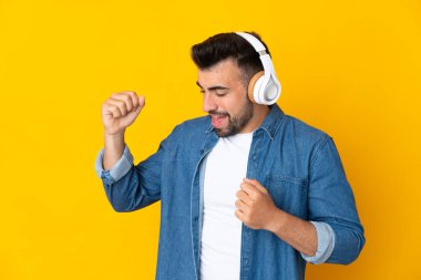İzole edilmiş sarı arka plan üzerinde beyaz bir adam müzik ve dans dinliyor.