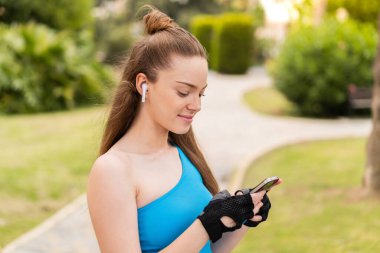 Açık havada giyinen, telefonlu müzik dinleyen güzel bir kız.