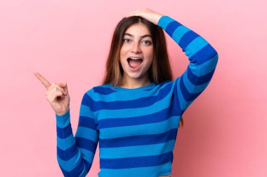 Pembe arka planda izole edilmiş beyaz bir kadın. Şaşırmış ve işaret ediyor.