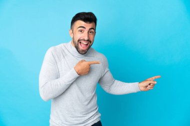 İzole edilmiş mavi arka planı olan beyaz bir adam şaşırmış ve işaret ediyor.
